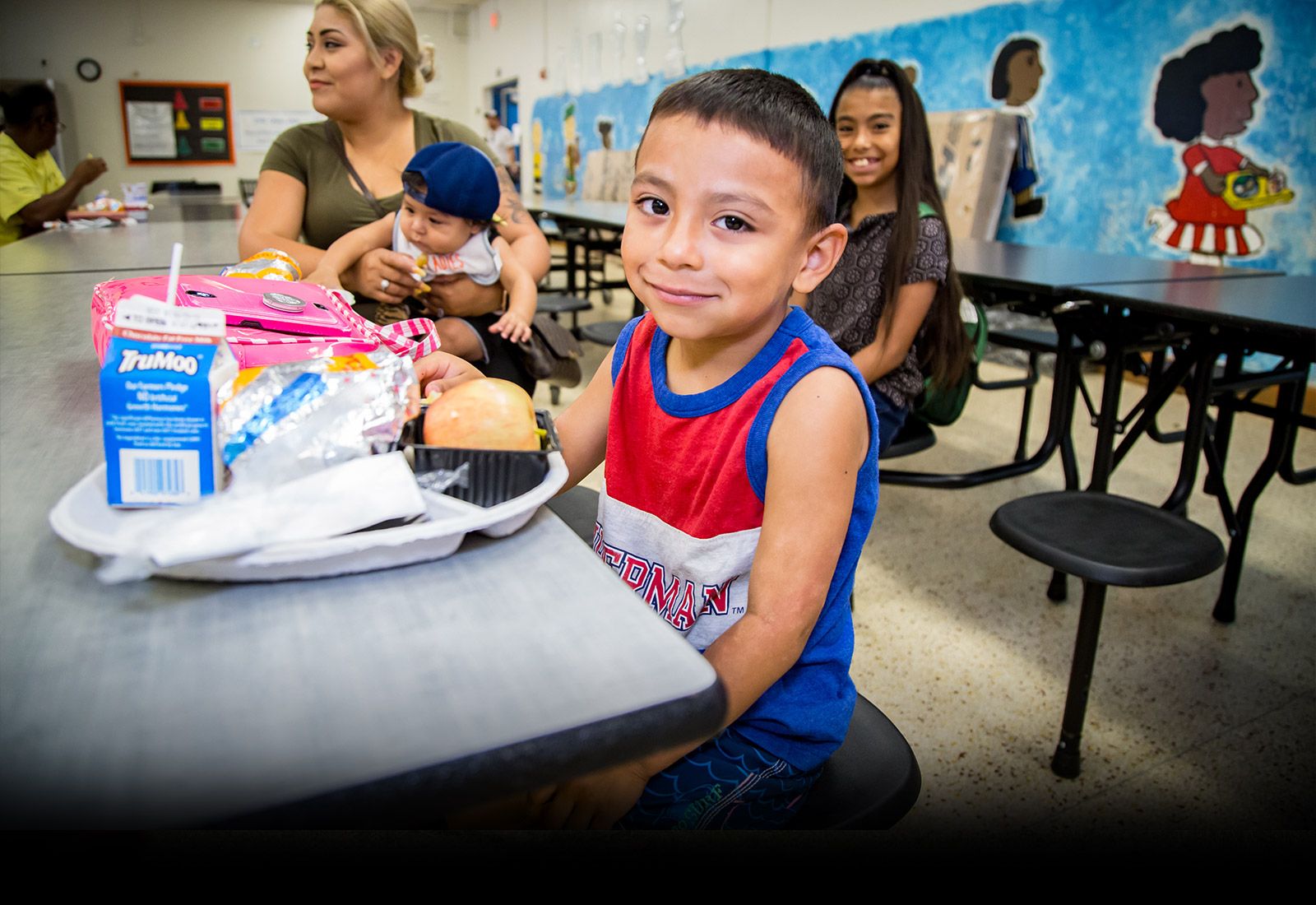hispanic boy sitting in a cafeteria with tray of food