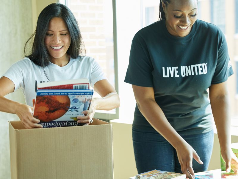 two women volunteers pack books in boxes