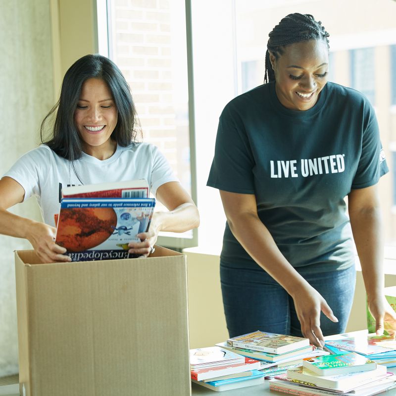 two women volunteers pack books in boxes