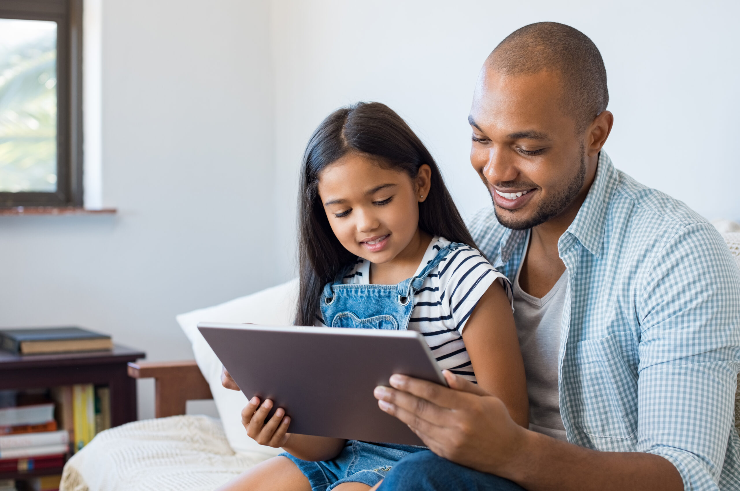 Father and daughter sitting on couch smiling at tablet