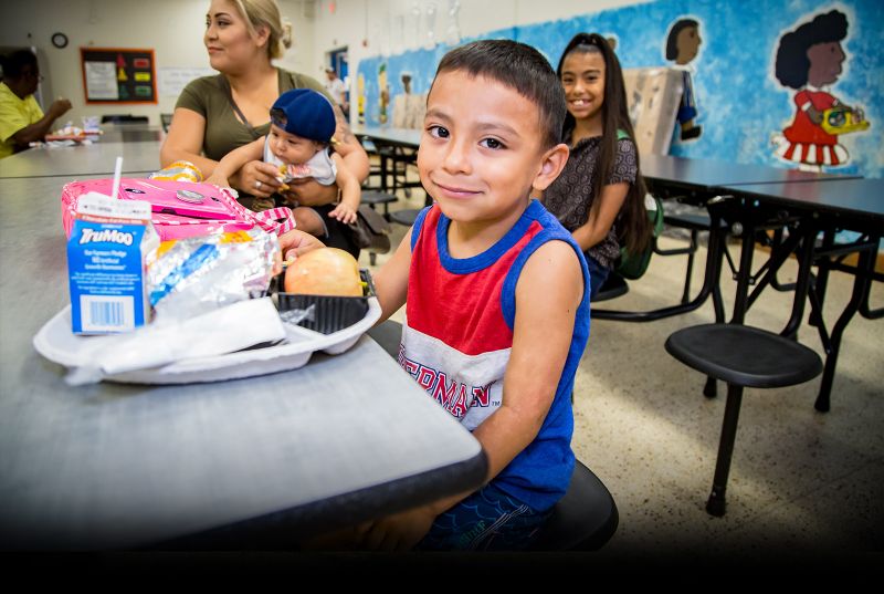 hispanic boy sitting in a cafeteria with tray of food